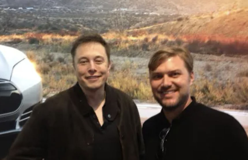 Elon Musk standing beside another person in front of a Tesla vehicle